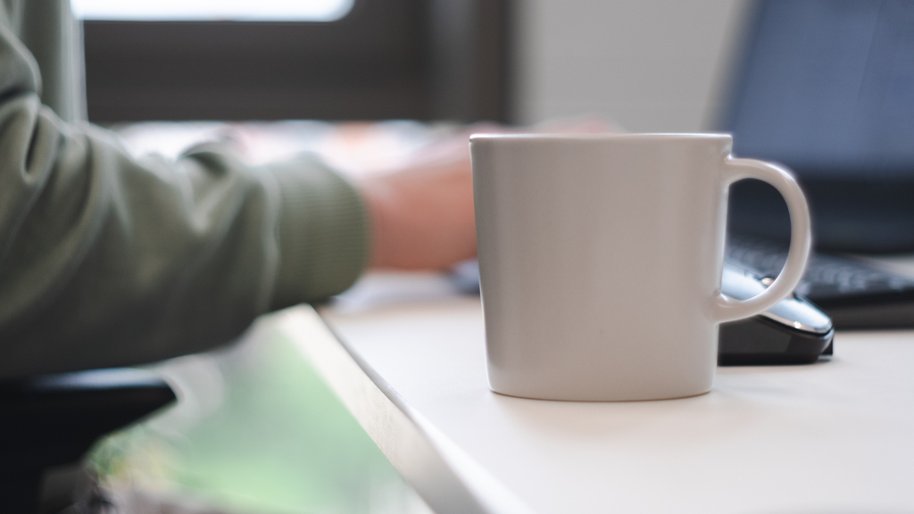 A coffee infront of a person working on a keyboard